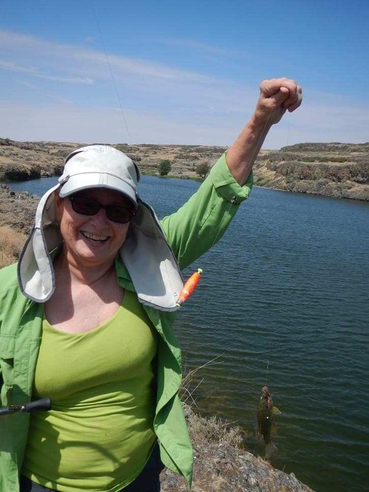 An angler in a wide-brimmed sun hat and sunglasses raising a rod